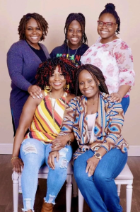 Susan Johnson smiles alongside her daughters in a professionally taken family portrait, posed against a tan backdrop.